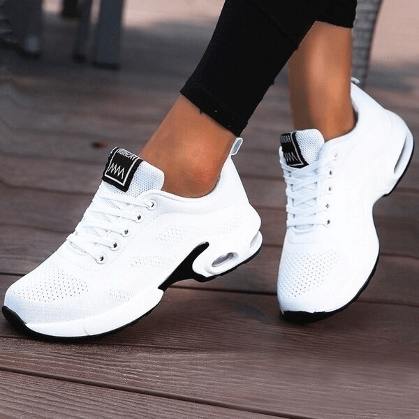 White breathable women's running shoes with lace-up closure on a wooden deck, showcasing flexibility and comfort.